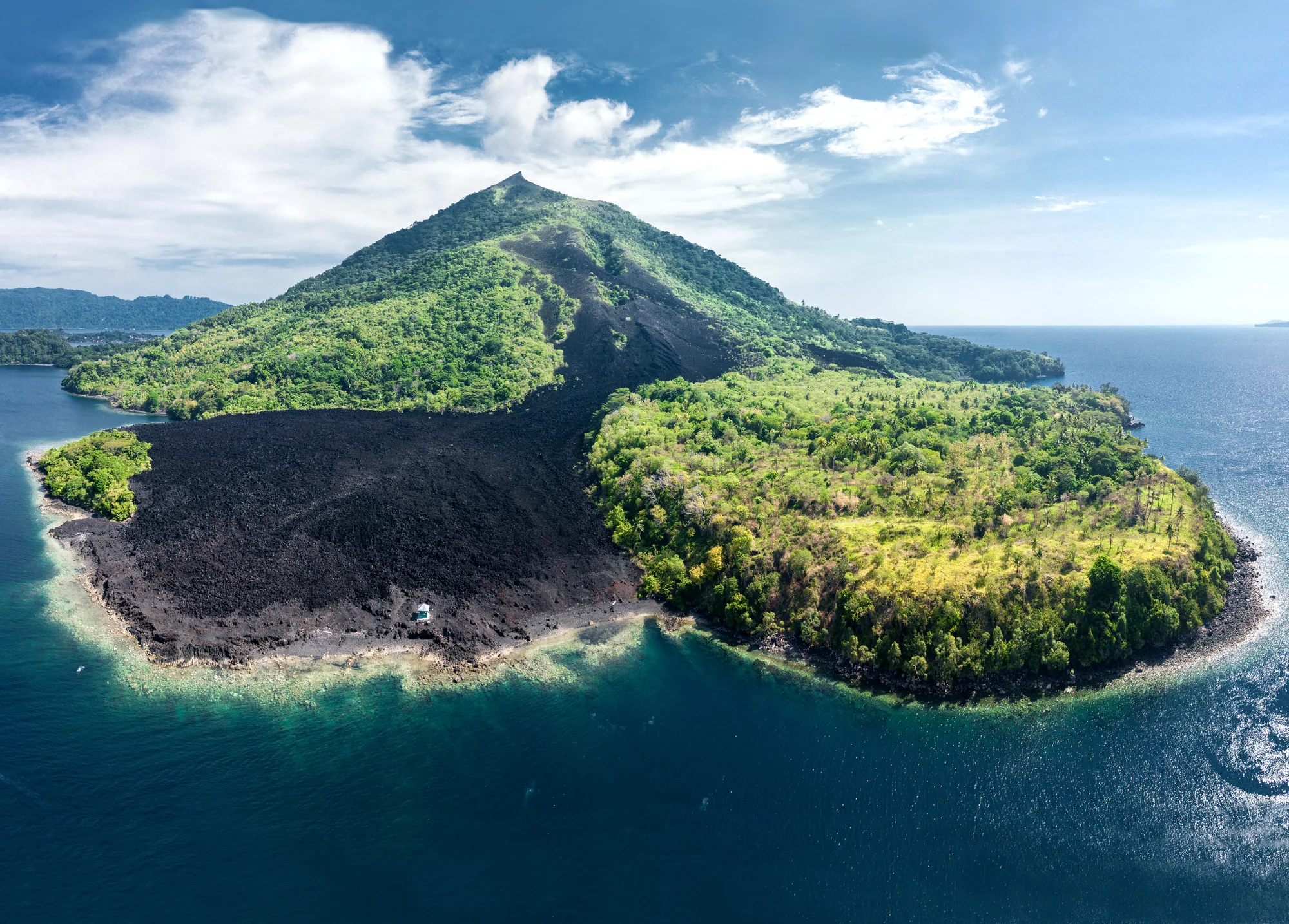 Aerial view of a cone-shaped hill with green vegetation and a broad dark band of bare ground extending to a curved shoreline.