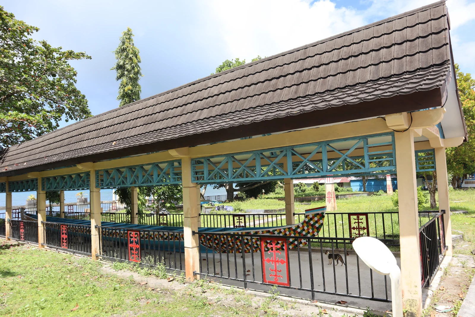 A long painted wooden boat rests inside an open pavilion with a tiled roof.